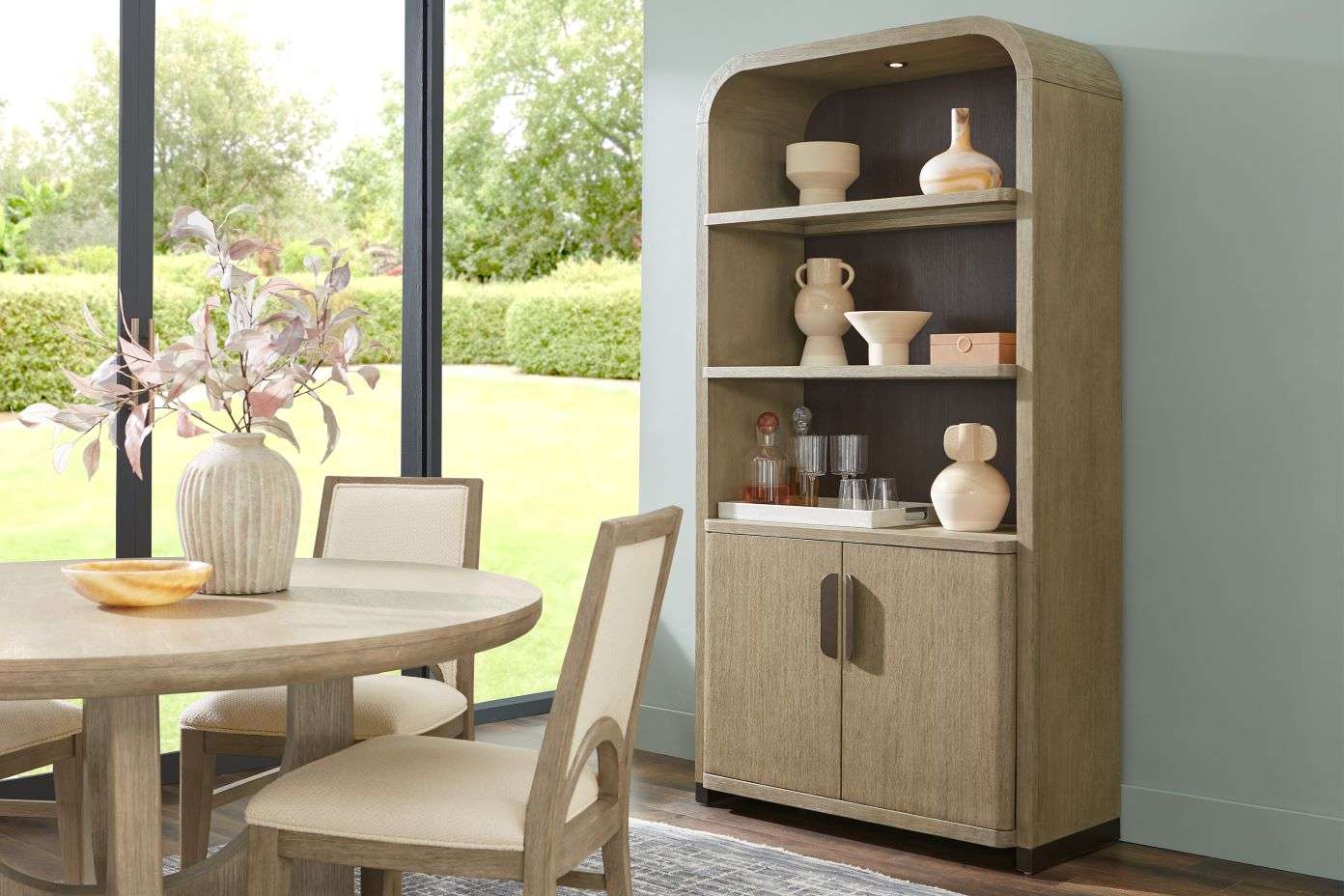 Wooden cabinet with shelves and doors, holding decorative items. Dining table and chairs in the foreground.

