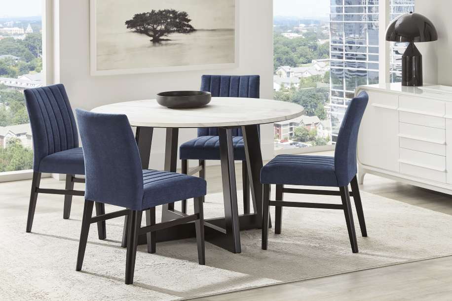 A dining room set with a round table, four blue chairs, and a white sideboard.
