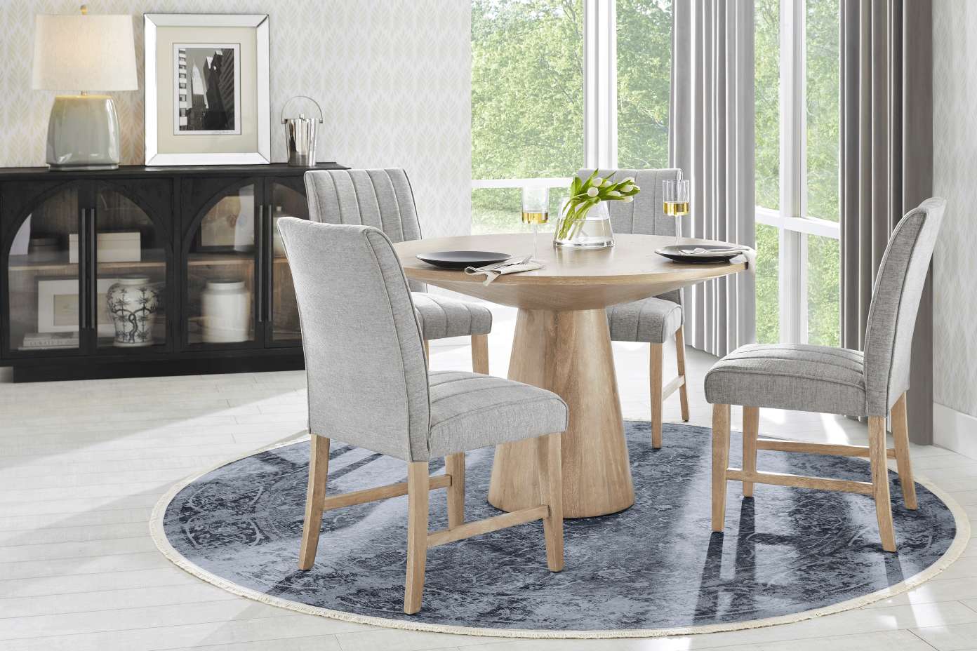 Dining room set with a round wooden table, gray chairs, and a patterned rug.
