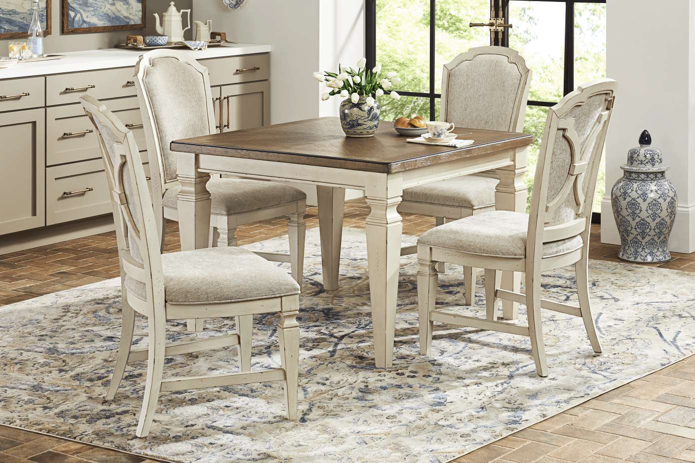Dining table with four chairs on a patterned rug.
