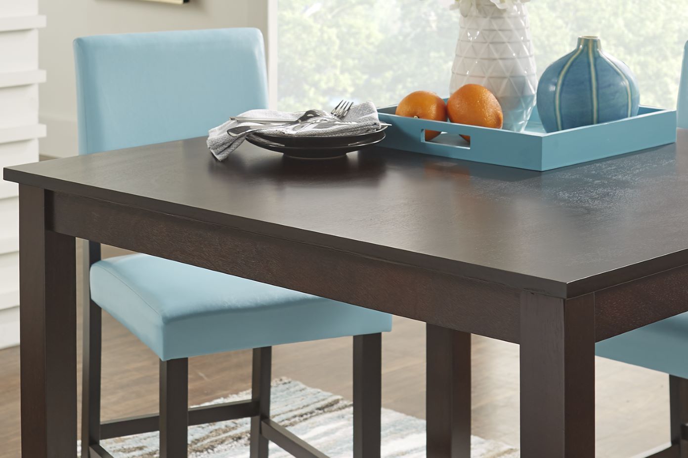 Dark brown dining table with blue chairs and a tray of oranges and vases.
