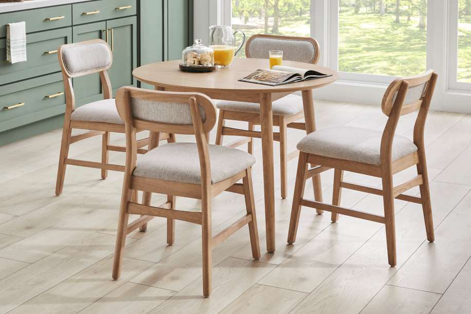 A round wooden dining table with four chairs. The chairs have light gray upholstered seats and backs.
