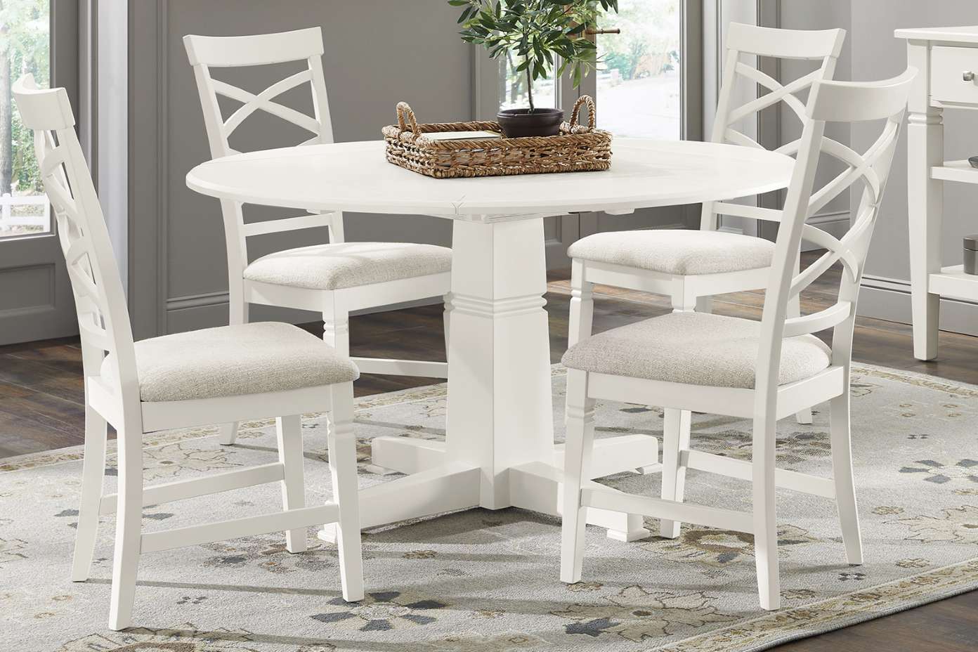 White round dining table with four white chairs and a woven basket centerpiece.