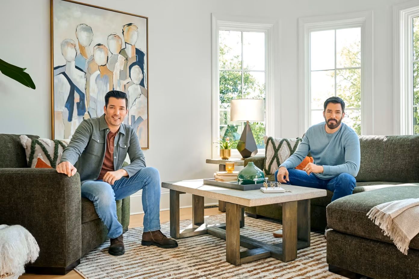 Two men sitting in a living room with a coffee table and artwork.
