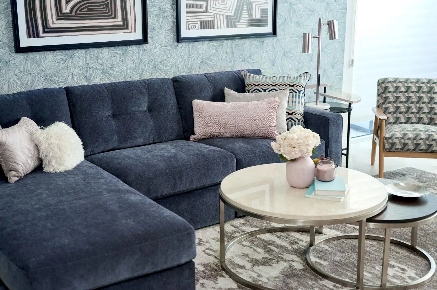 Blue sectional sofa with decorative pillows, round coffee tables, and a patterned armchair.
