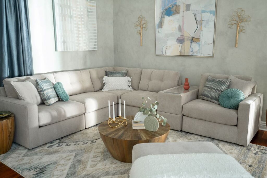 A beige sectional sofa with decorative pillows, a wooden coffee table, and a patterned rug.
