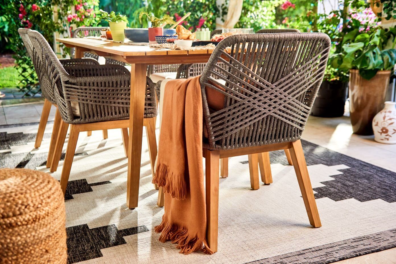 Outdoor dining set with woven chairs and a fringed blanket.
