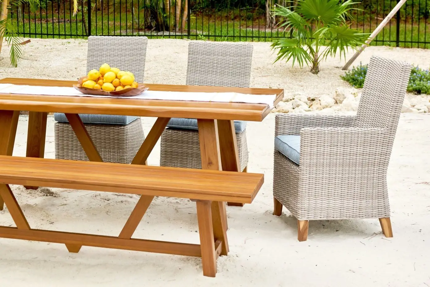 Wooden outdoor dining set with woven chairs and a bench. A bowl of lemons sits on the table.
