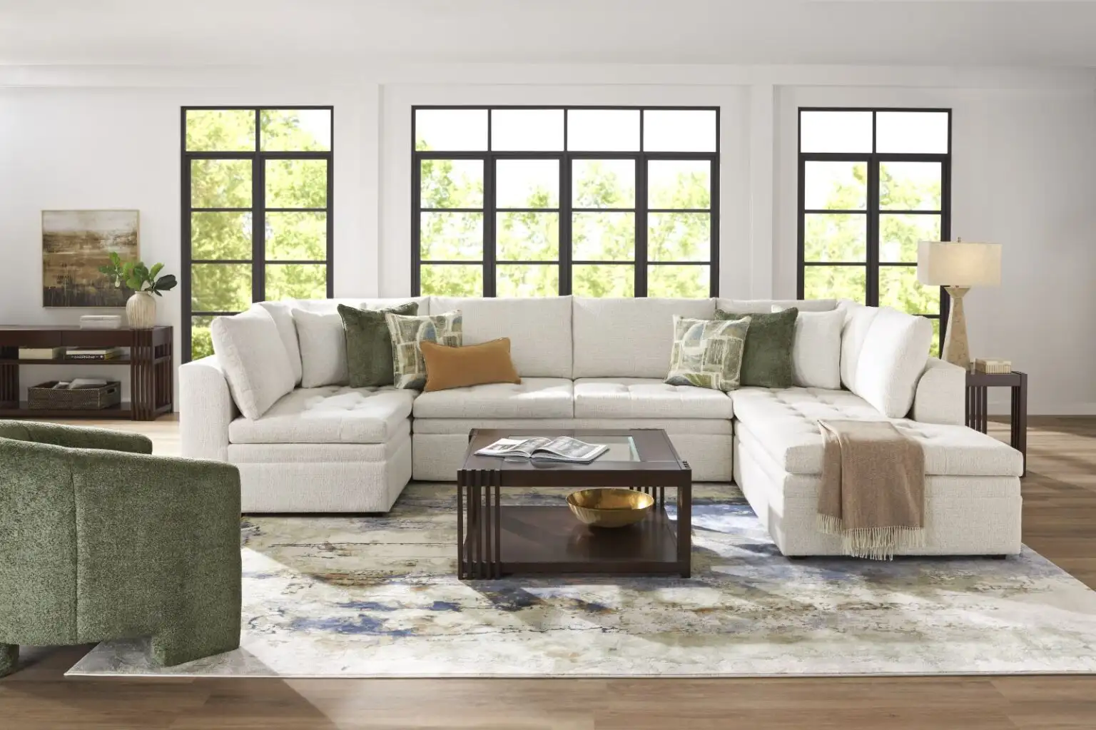 A large white sectional sofa with green and tan accent pillows, a dark wood coffee table, and a green armchair.
