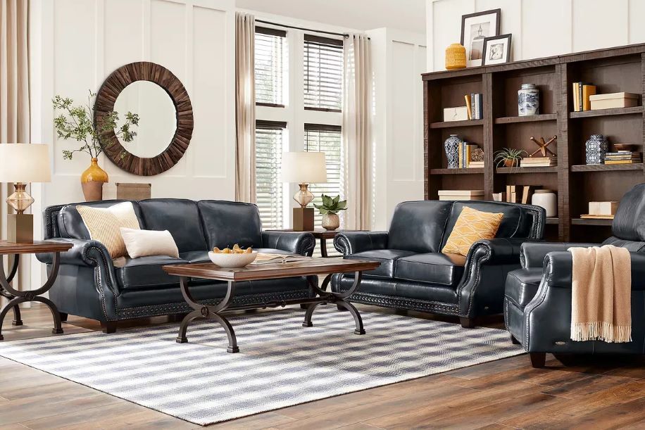 Living room with blue leather furniture, a striped rug, and a wooden bookshelf.
