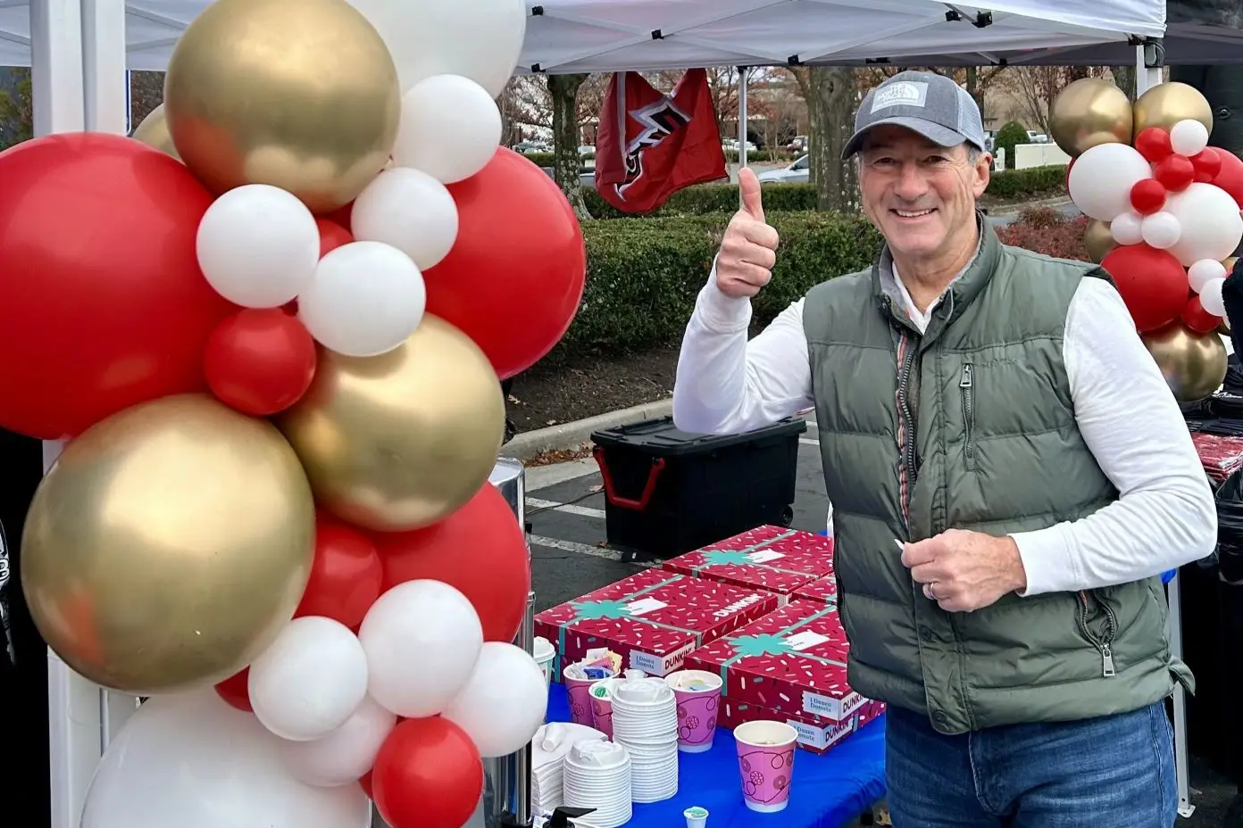 Man giving a thumbs up next to balloons and Dunkin' Donuts boxes.
