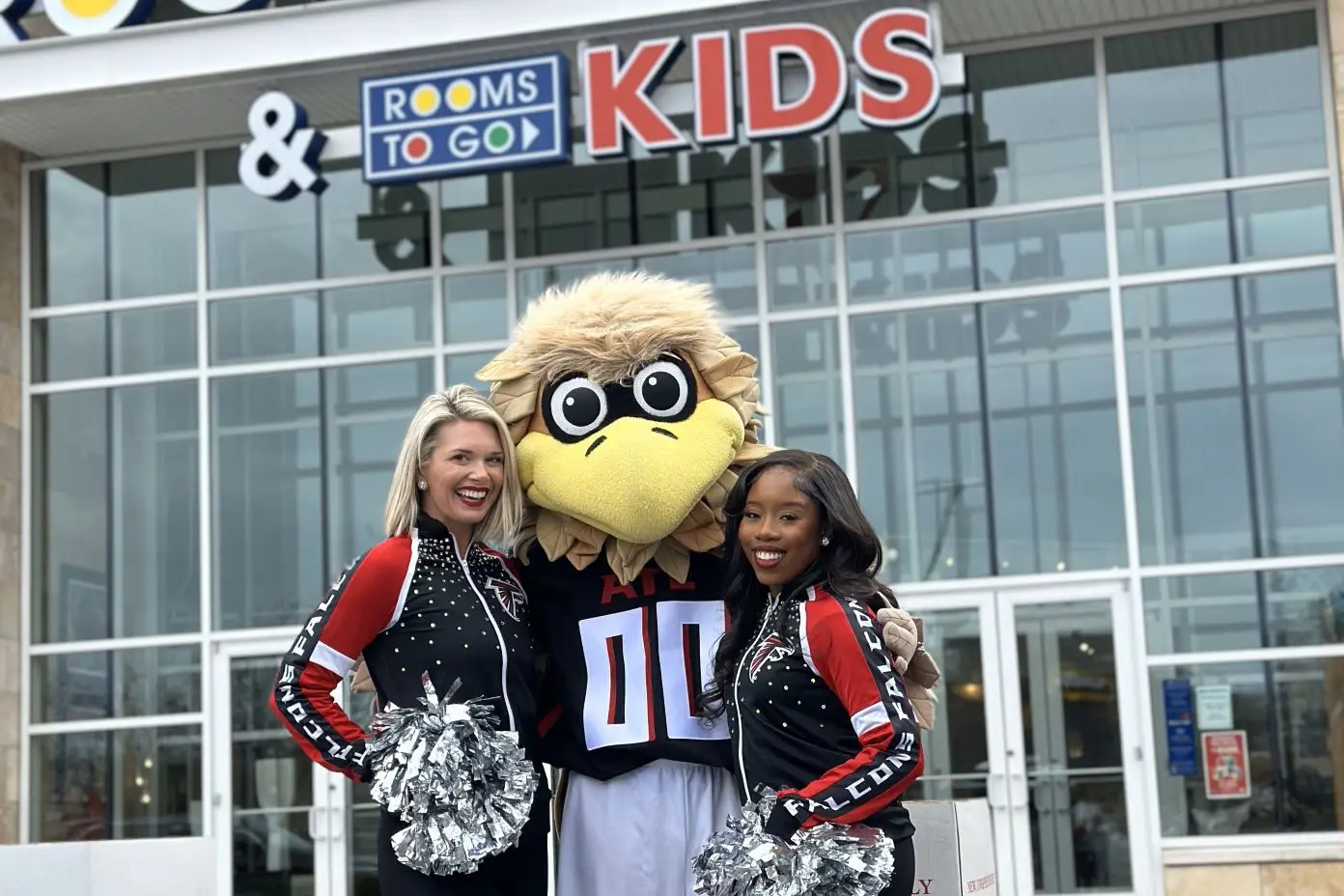 Rooms to Go & Kids. Two cheerleaders and a mascot pose in front of a store.

