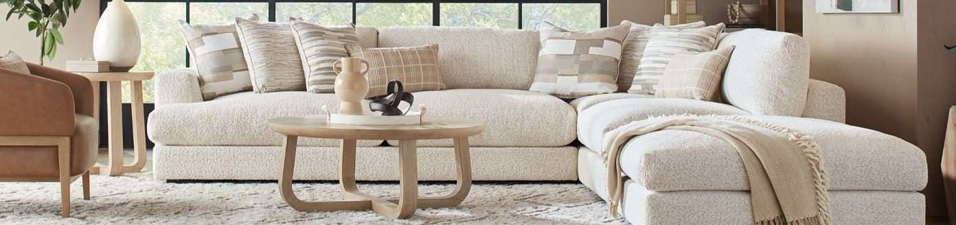 Cream-colored sectional sofa with patterned pillows and a wooden coffee table.