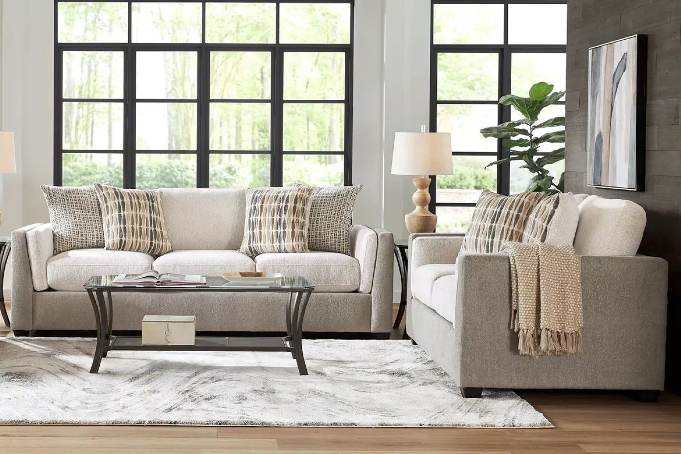 Living room with a light-colored sofa, armchair, and coffee table. Large windows and a rug are also present.

