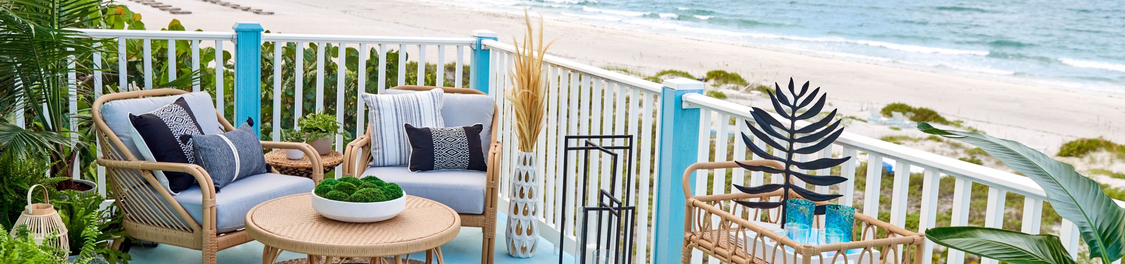 A beachside balcony with wicker furniture, pillows, and ocean views.