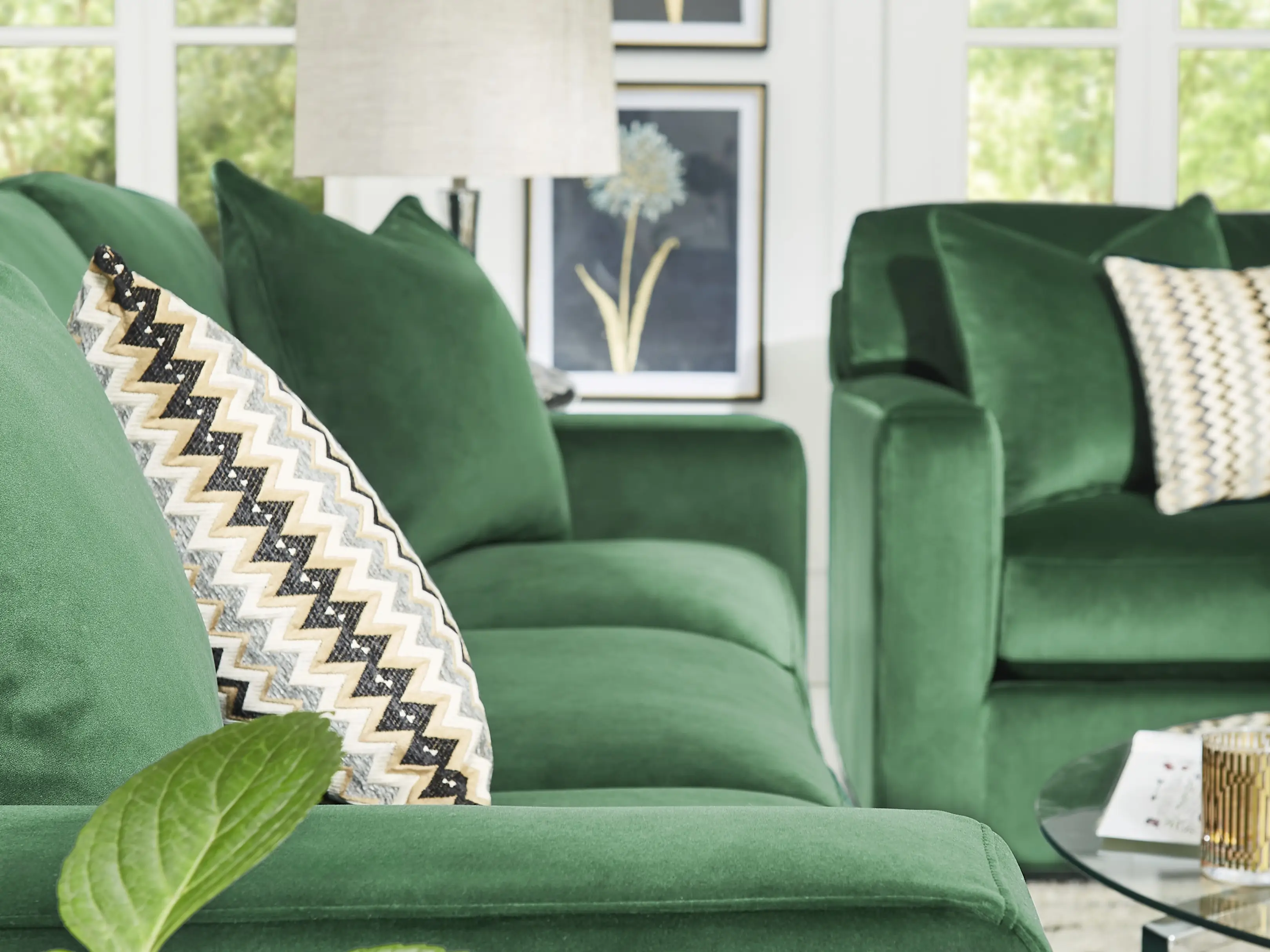 A close-up of a plush green velvet sofa with a patterned chevron throw pillow, featuring a modern living room setting.