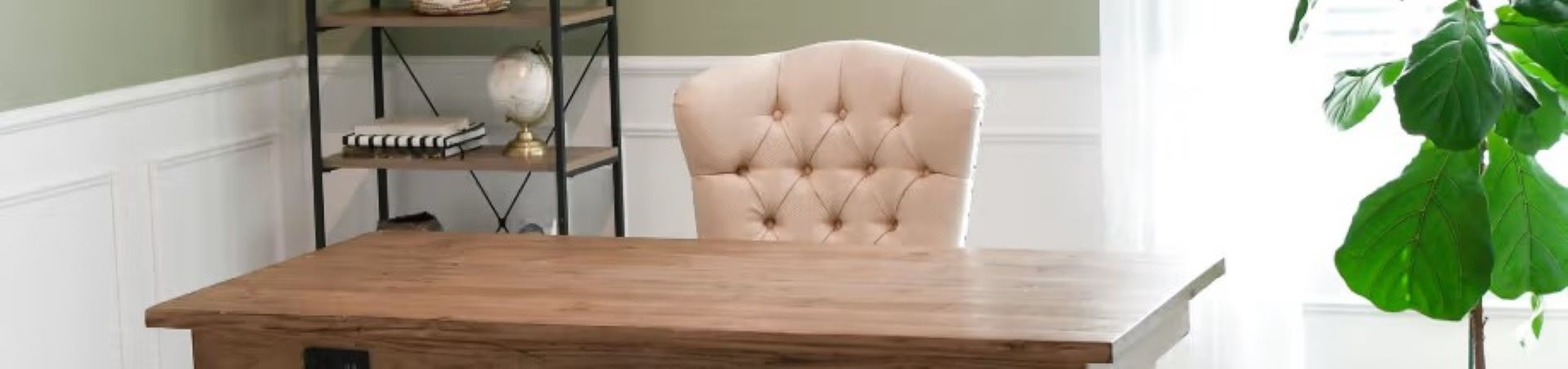 Wooden desk with a tufted beige chair in front of it. A bookshelf and a plant are in the background.