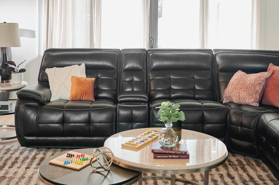 Black leather sectional sofa with throw pillows and coffee tables.
