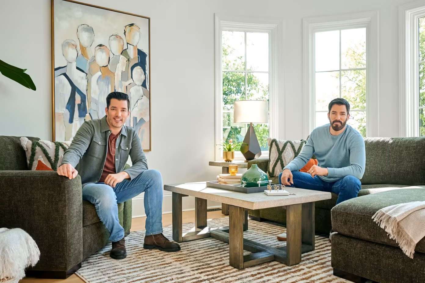 Two men sitting in a living room with a coffee table and artwork.
