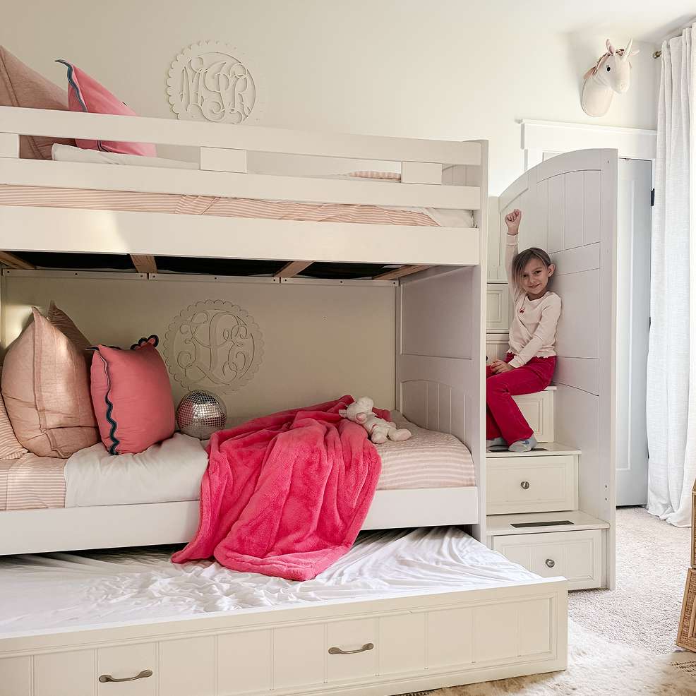 A white bunk bed with a pull-out trundle bed, a girl sitting on the stairs.
