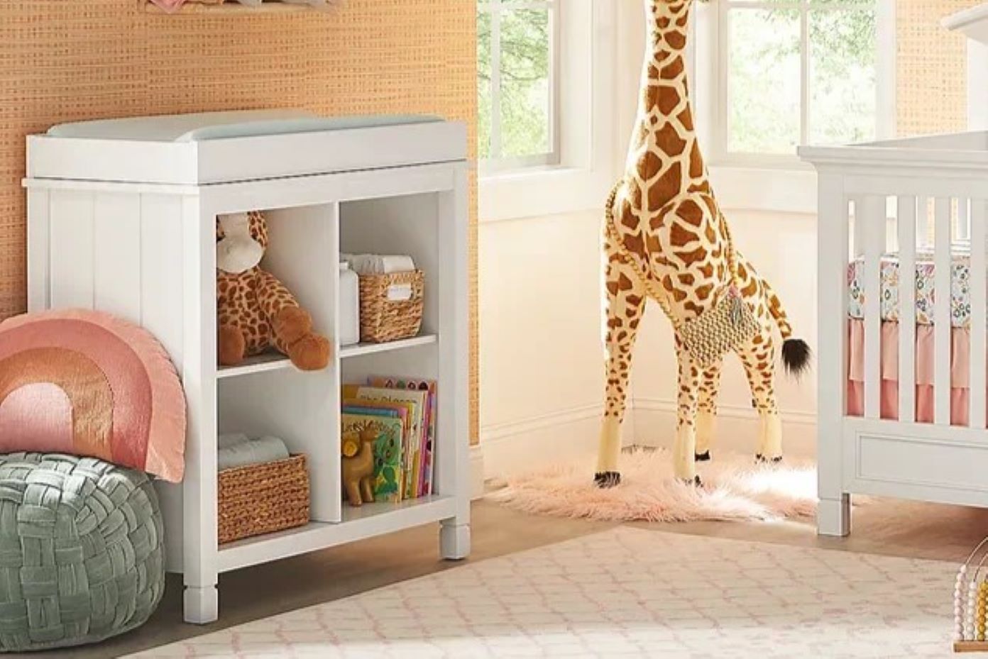White changing table with shelves, giraffe stuffed animal, and crib.
