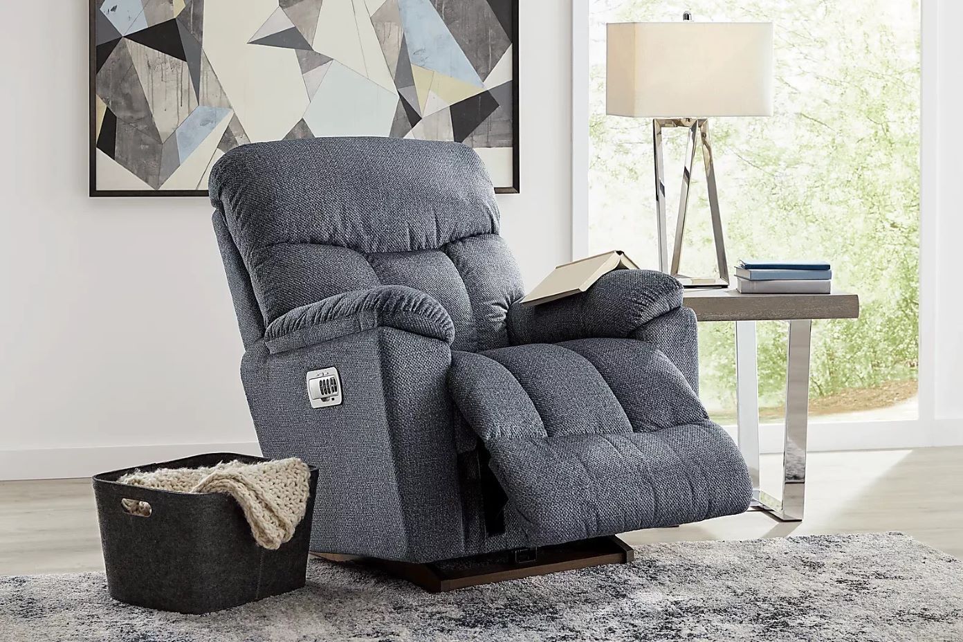 Blue recliner chair with a book on the arm, next to a side table with a lamp.
