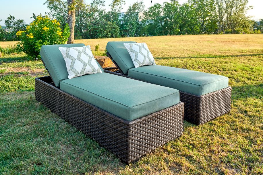 Two outdoor chaise lounges with teal cushions and decorative pillows on a grassy lawn.
