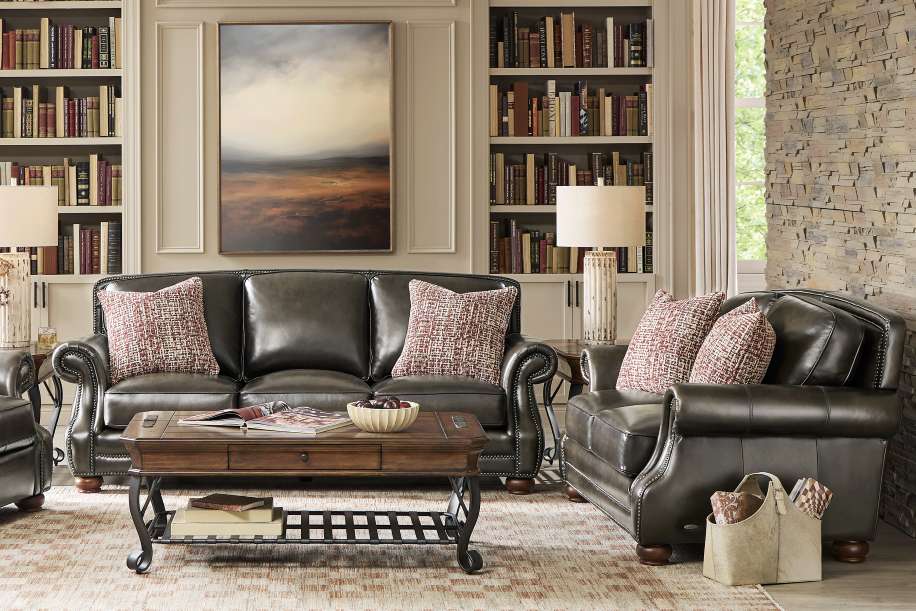 Living room with leather sofa, armchair, coffee table, bookshelves, and artwork.
