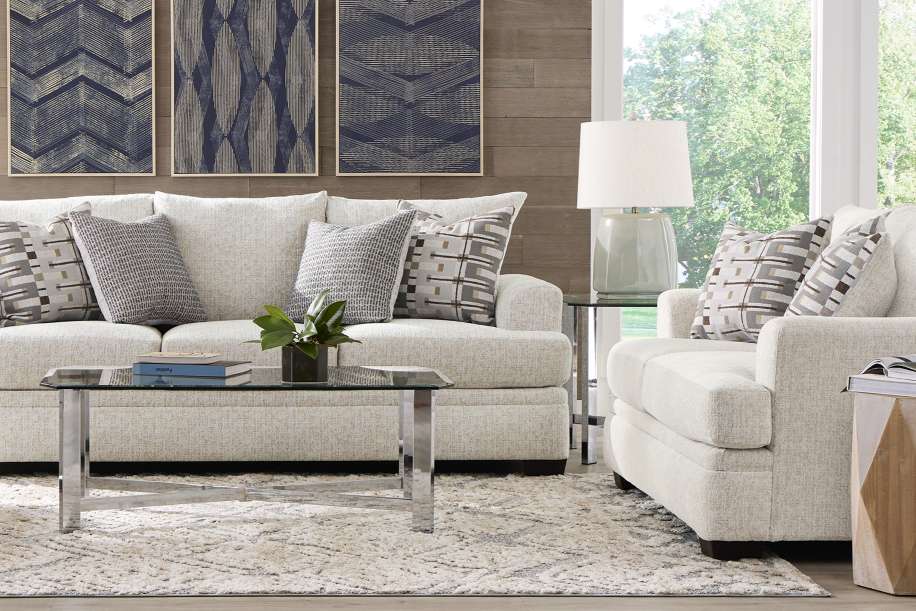 Living room with a light-colored sofa, armchair, and coffee table. Decorative pillows and artwork are present.
