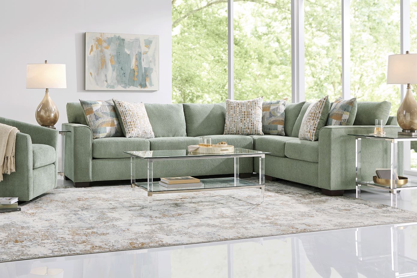 Green sectional sofa with patterned pillows and a glass coffee table.
