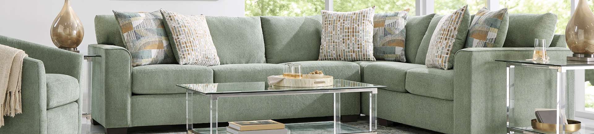 Green sectional sofa with patterned throw pillows and a glass coffee table.