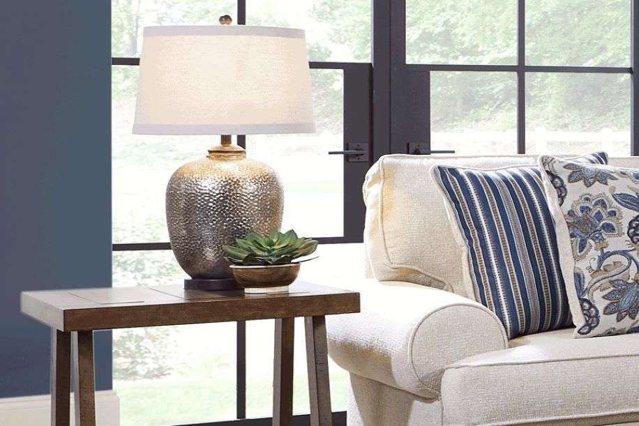 A lamp on a side table next to a couch with pillows.
