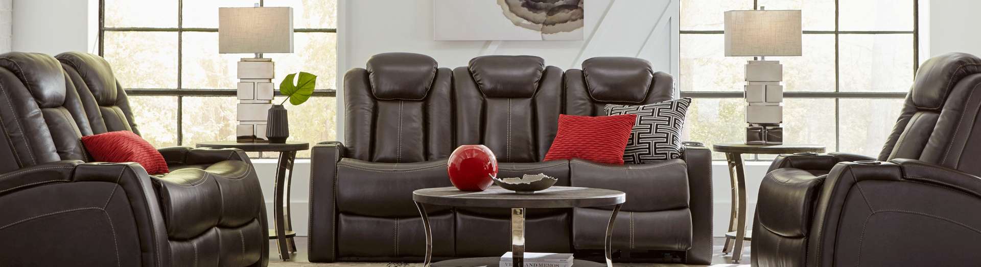 Brown leather reclining sofa with red and black pillows, and side tables with lamps.
