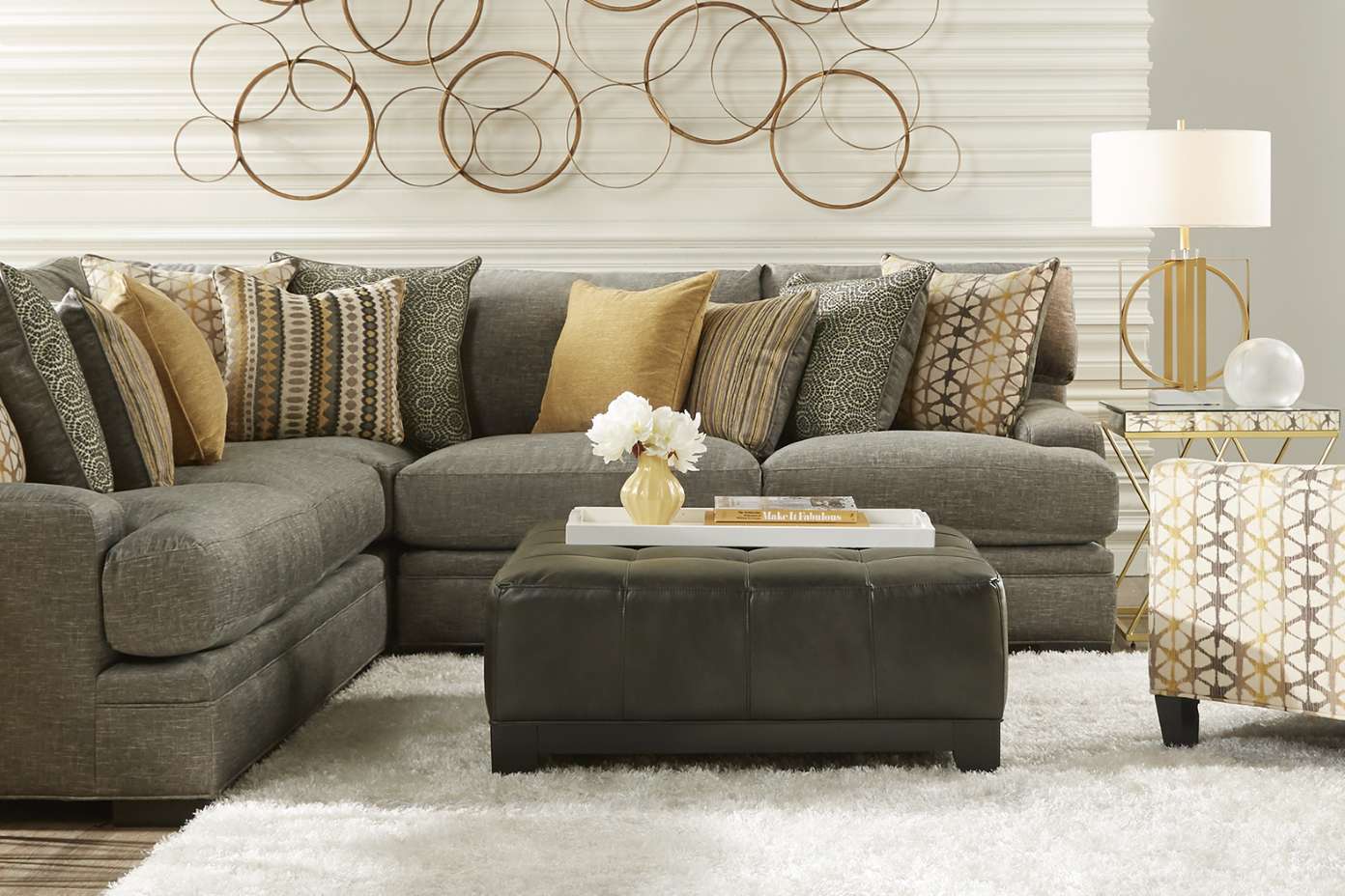 Gray sectional sofa with decorative pillows, ottoman, and a white fluffy rug.
