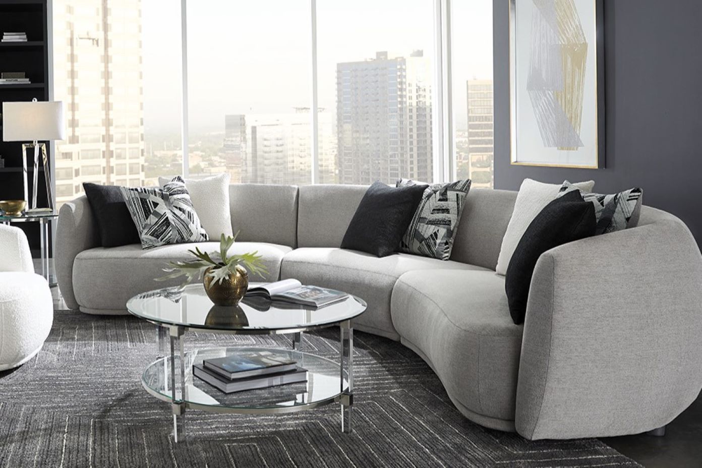 Curved gray sectional sofa with decorative pillows and a glass coffee table.
