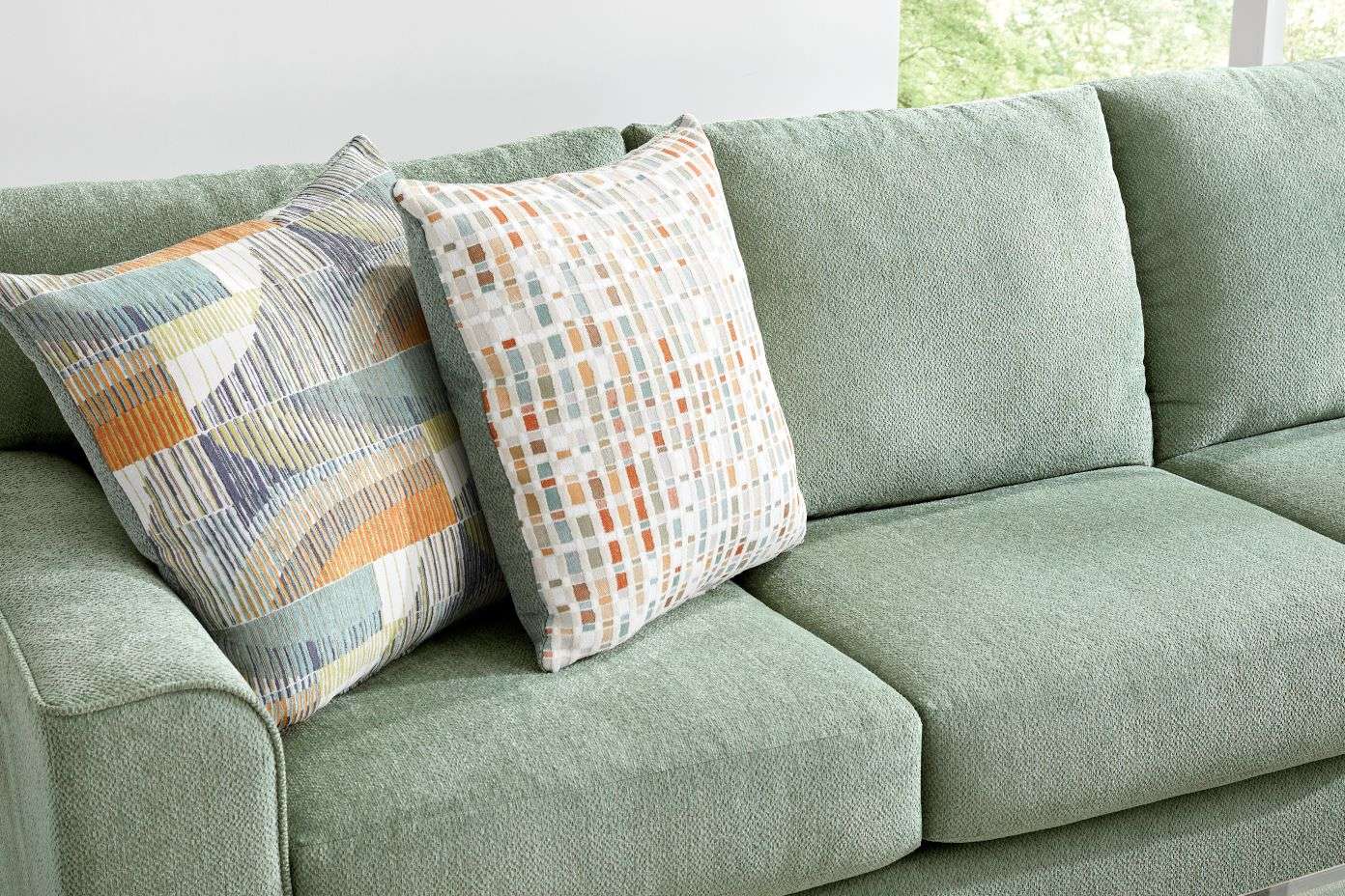 A light green sofa with two patterned pillows.
