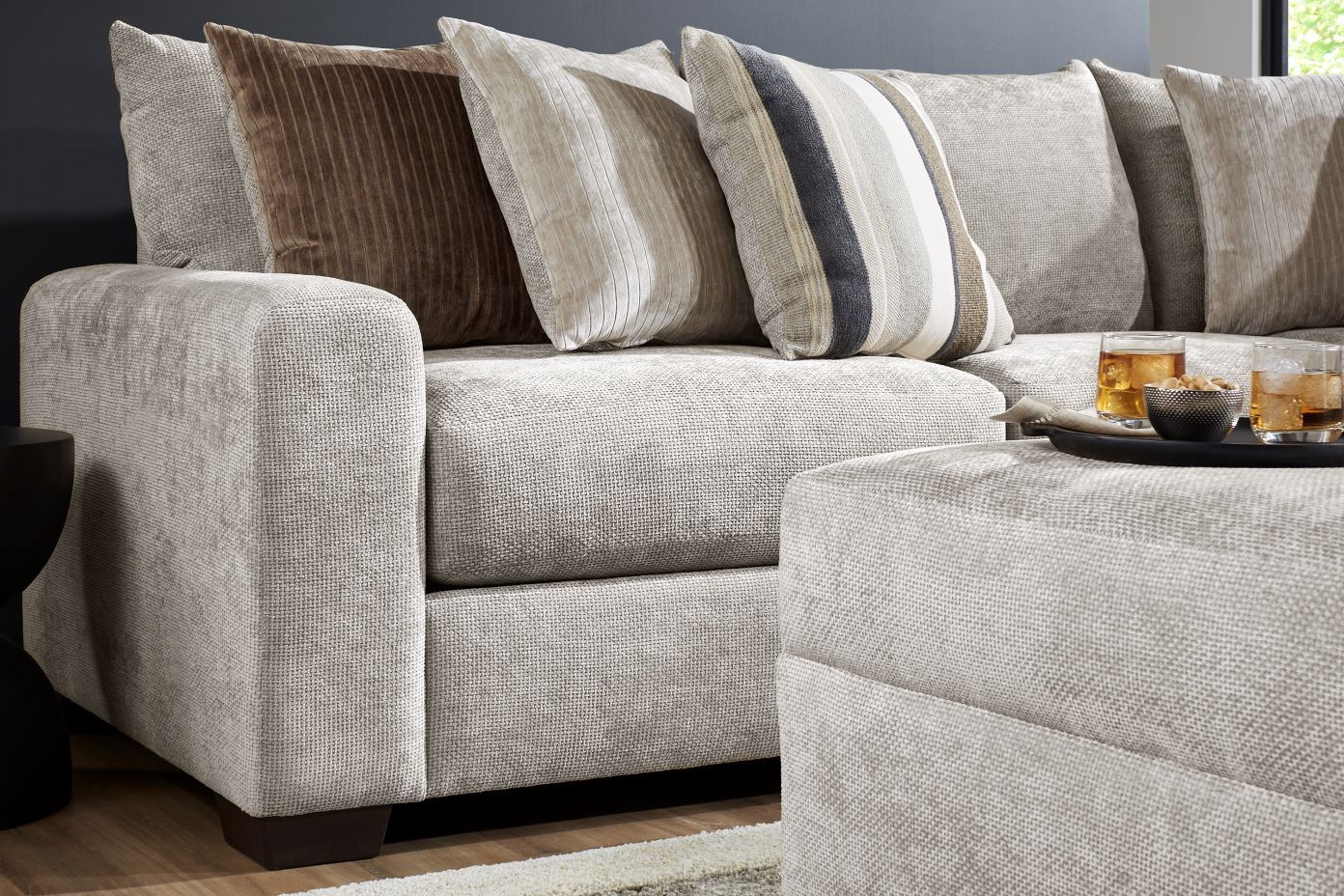 A light gray sectional sofa with pillows and a tray of drinks and snacks.
