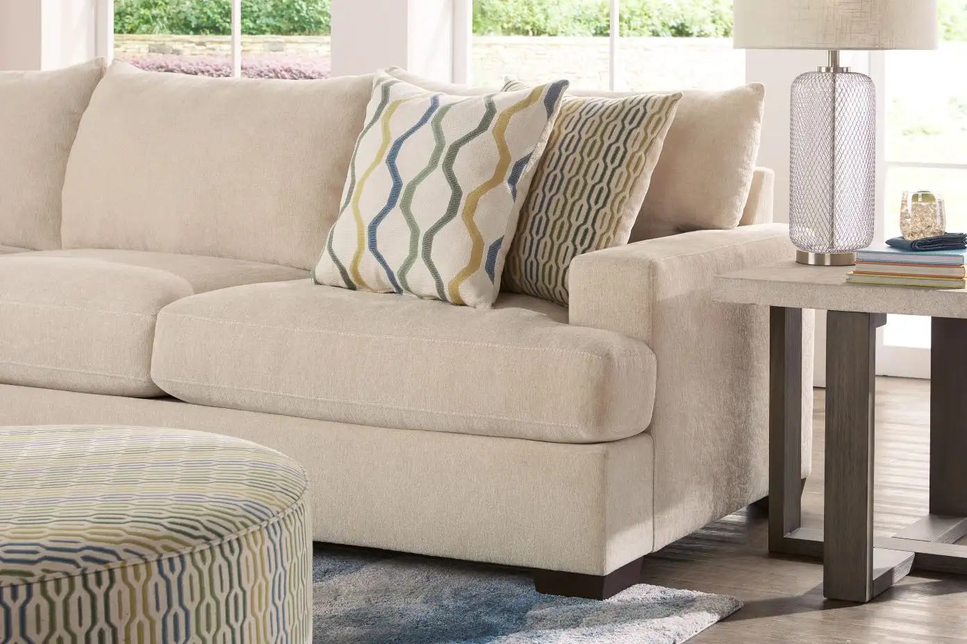 Beige sectional sofa with patterned throw pillows and a side table with a lamp.
