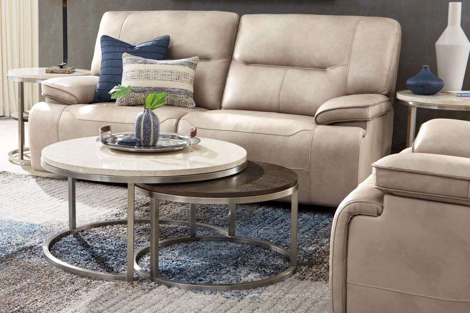 Beige leather sofa with two round coffee tables and a patterned rug.
