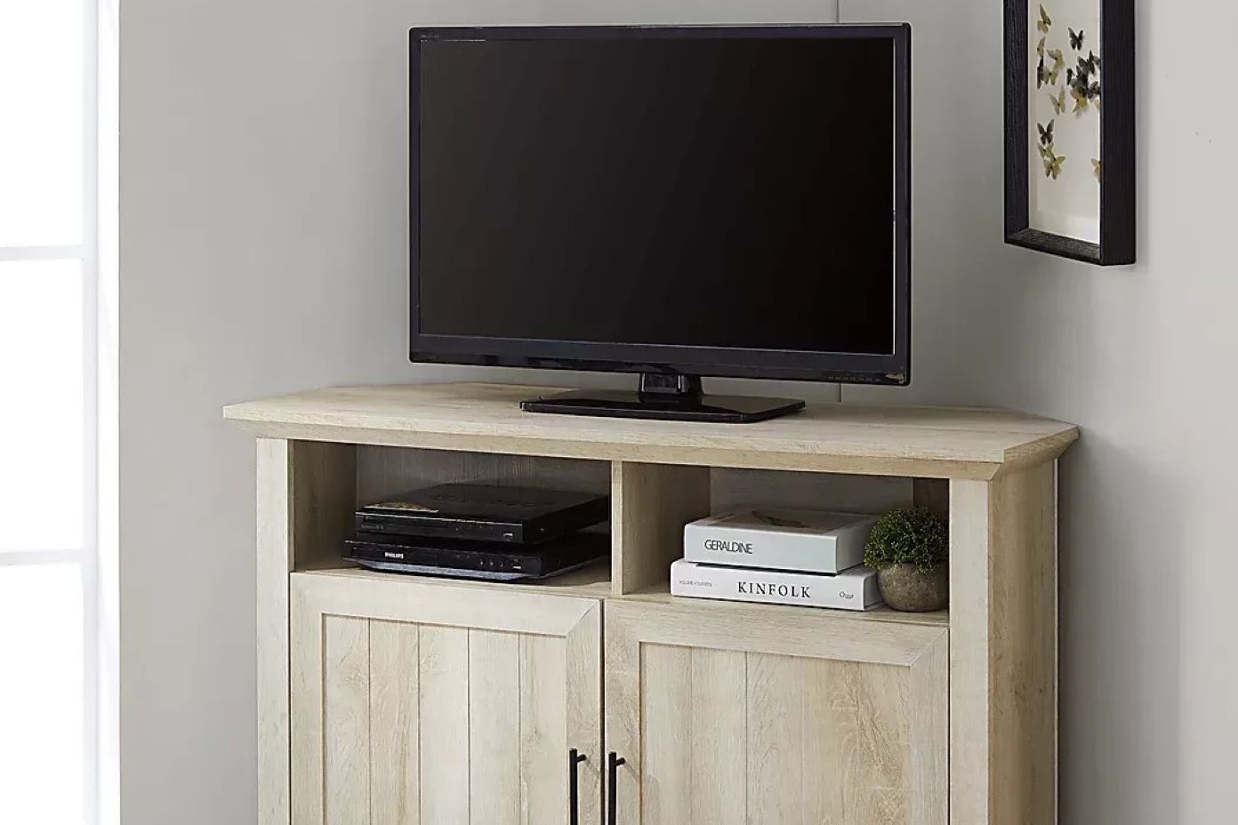 A light-colored wooden corner TV stand with a TV on top.
