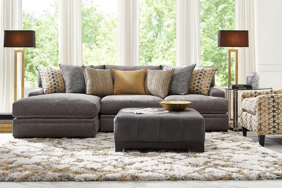 Gray sectional sofa with patterned pillows, ottoman, and rug.
