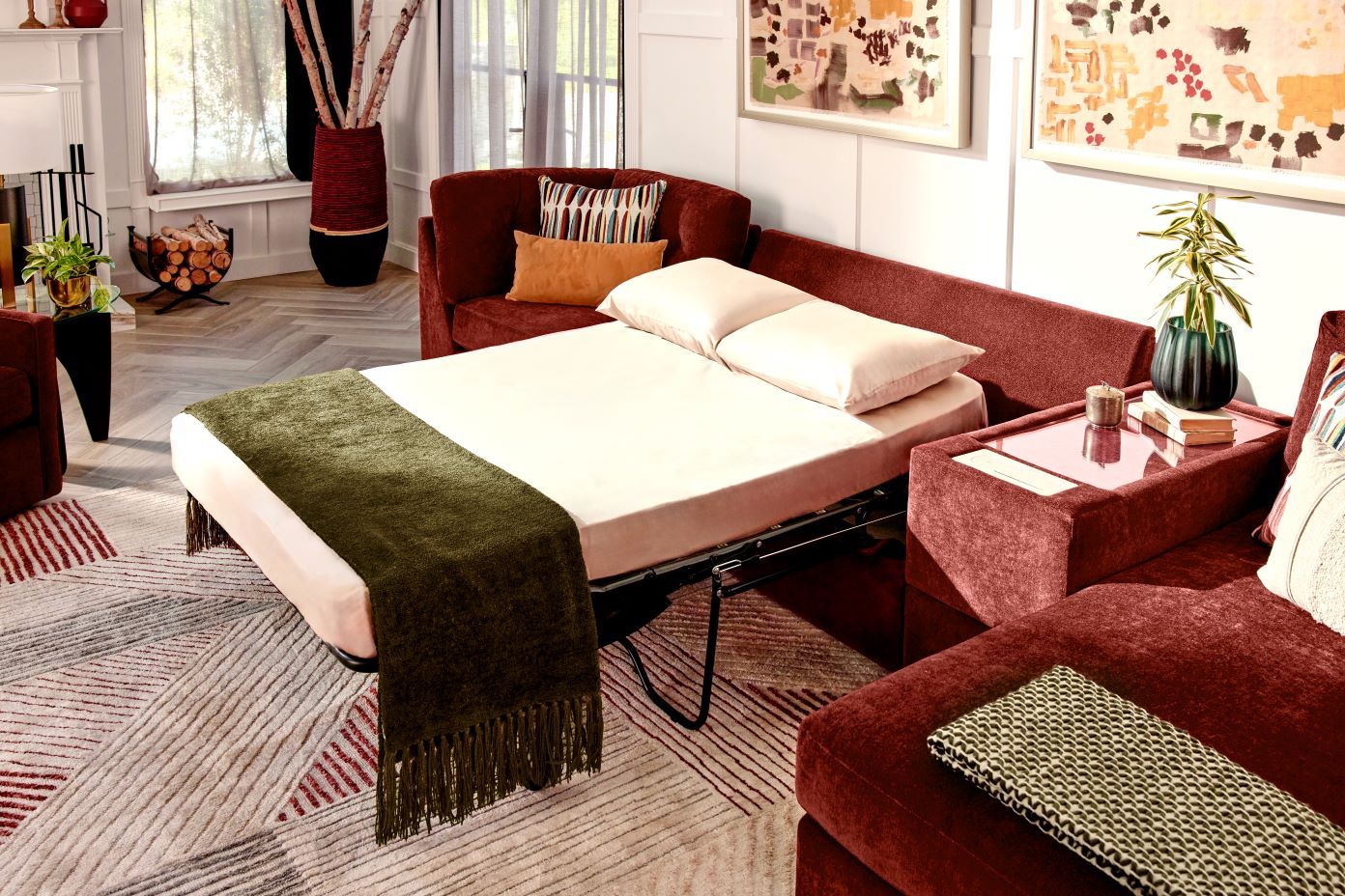A red sectional sofa with a pull-out bed, a green throw blanket, and pillows.
