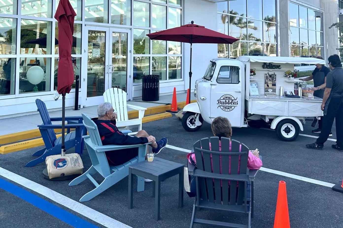 A white food truck with the name "Bubbles" parked outside a building, with people sitting in chairs.
