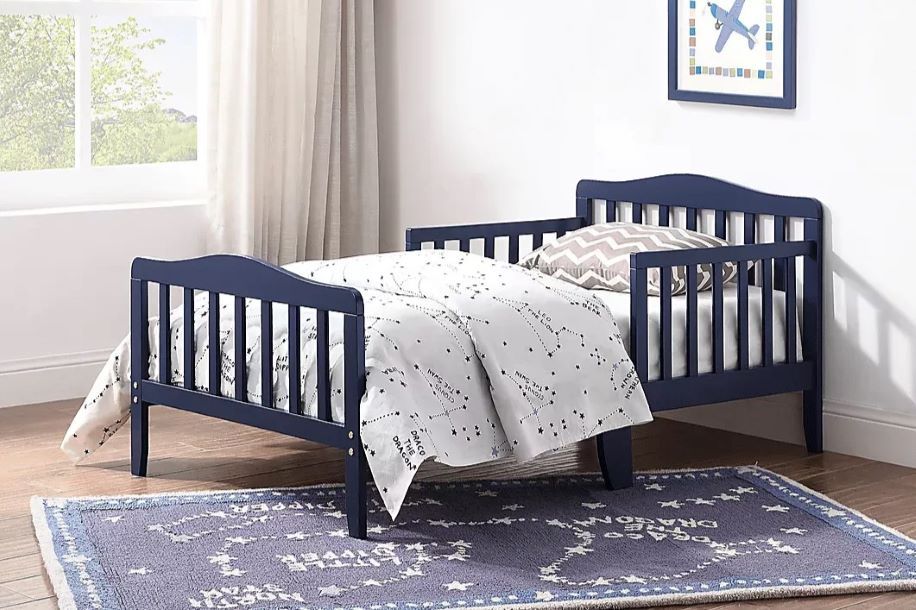 Navy blue toddler bed with a constellation-themed blanket and rug.
