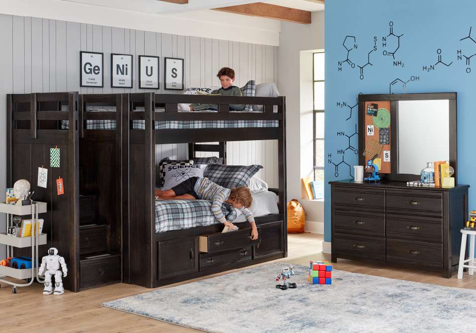 A bunk bed with two boys, a dresser, and a rug.
