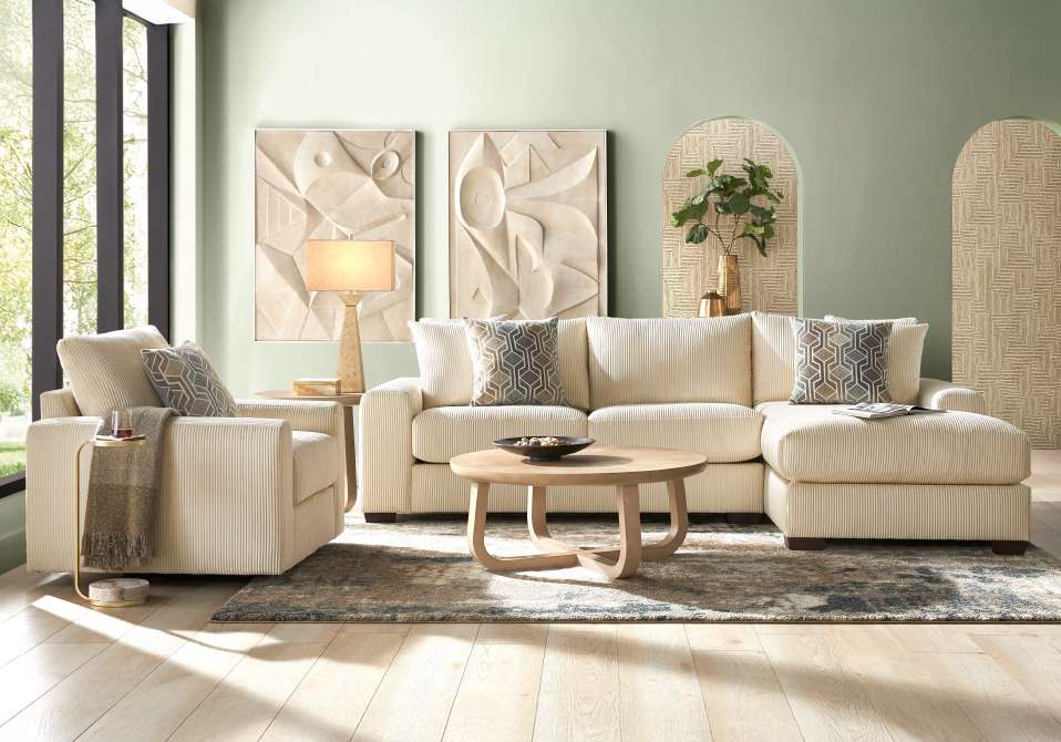 Cream-colored sectional sofa with patterned pillows, a round wooden coffee table, and abstract wall art.
