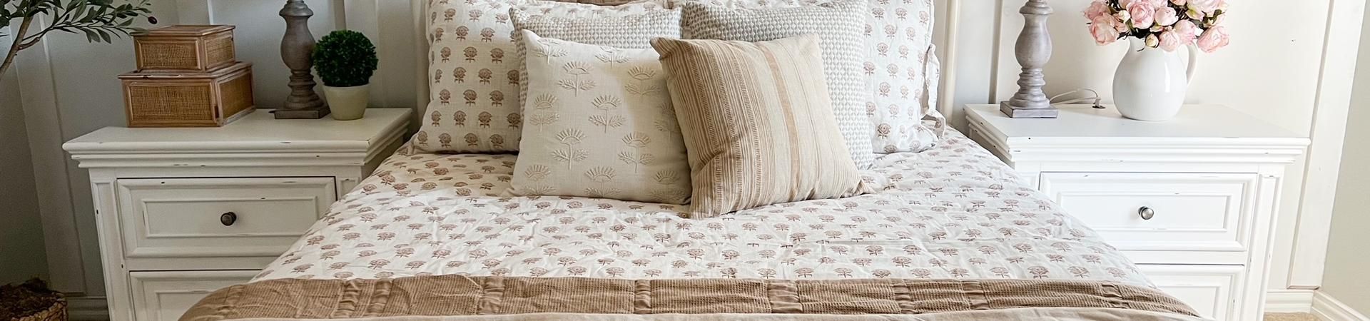 A bed with white nightstands, lamps, and decorative pillows.
