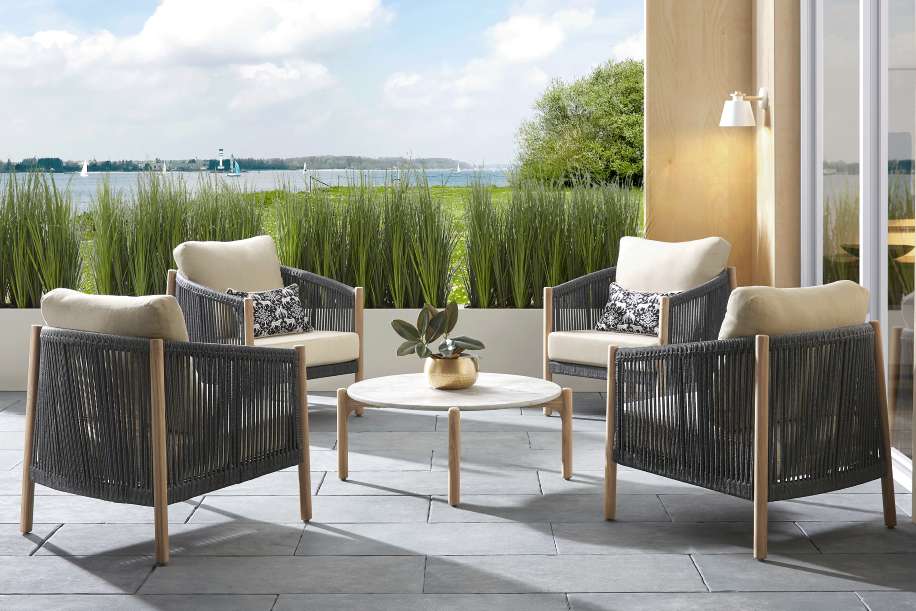 Four outdoor armchairs with gray rope detailing and beige cushions arranged around a round marble coffee table.
