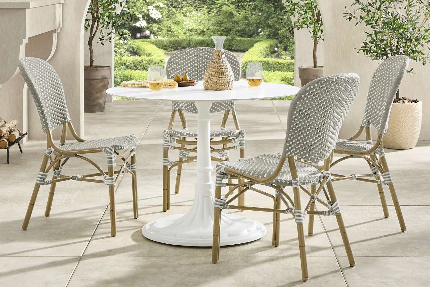 A white round outdoor dining table with four gray and white woven chairs.
