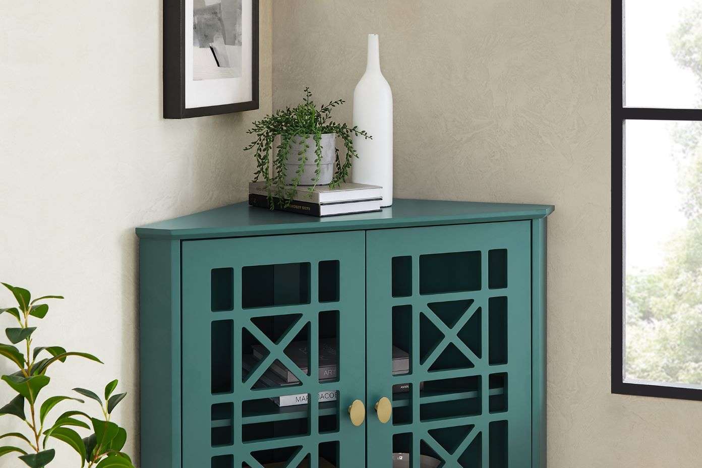 Teal corner cabinet with geometric door design, topped with decor.
